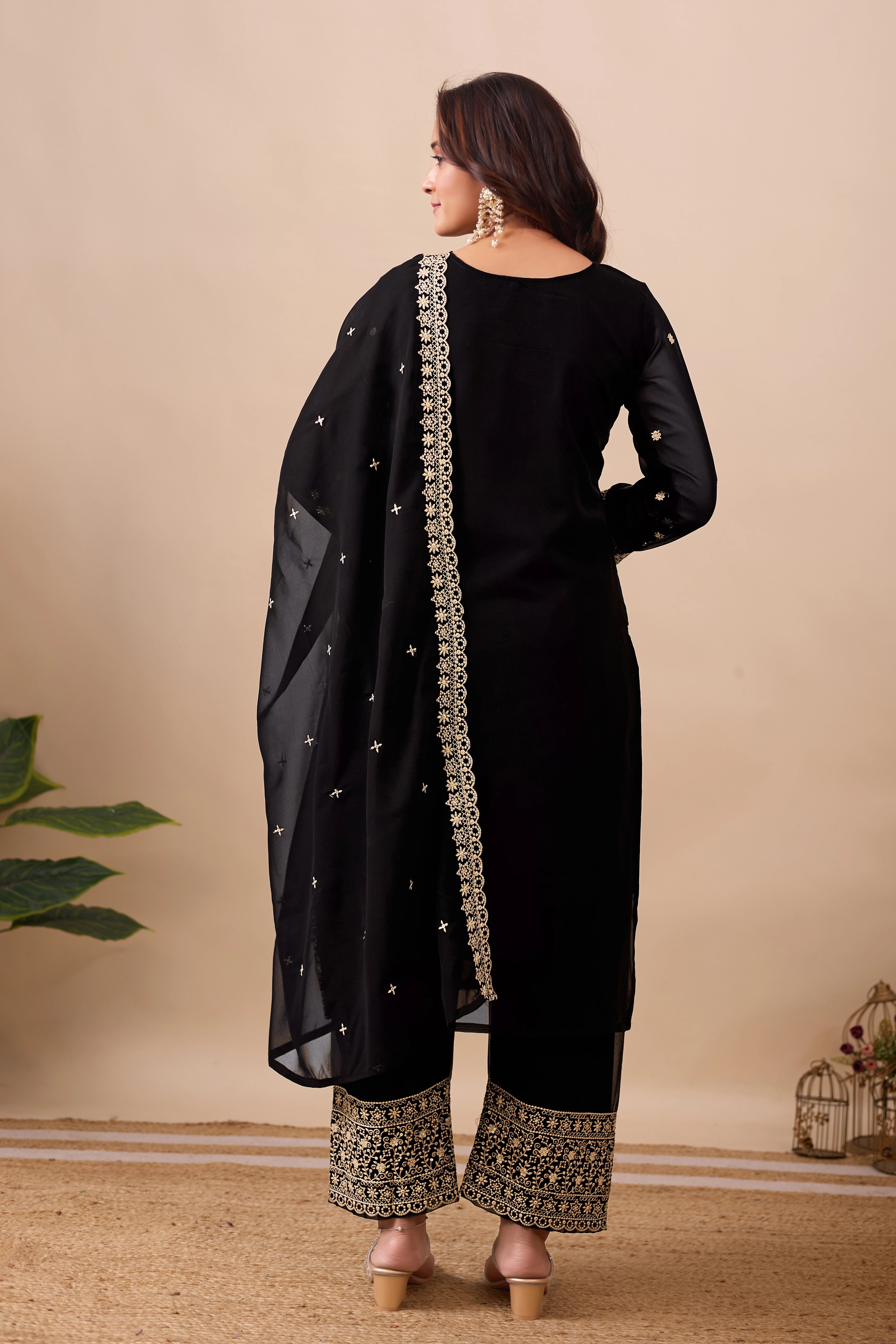 Woman wearing a black traditional outfit with gold embroidery on a beige background